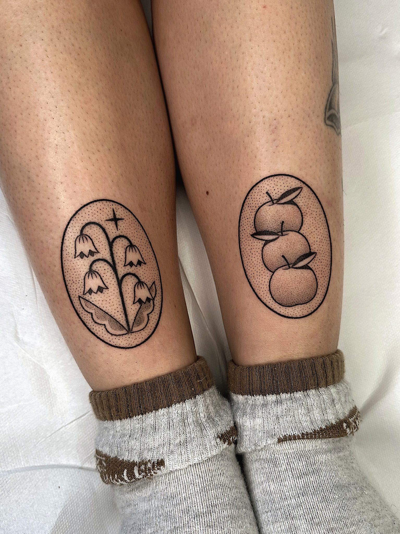 Tatouages handpoke en médaillon sur les deux mollets, fleurs et fruits