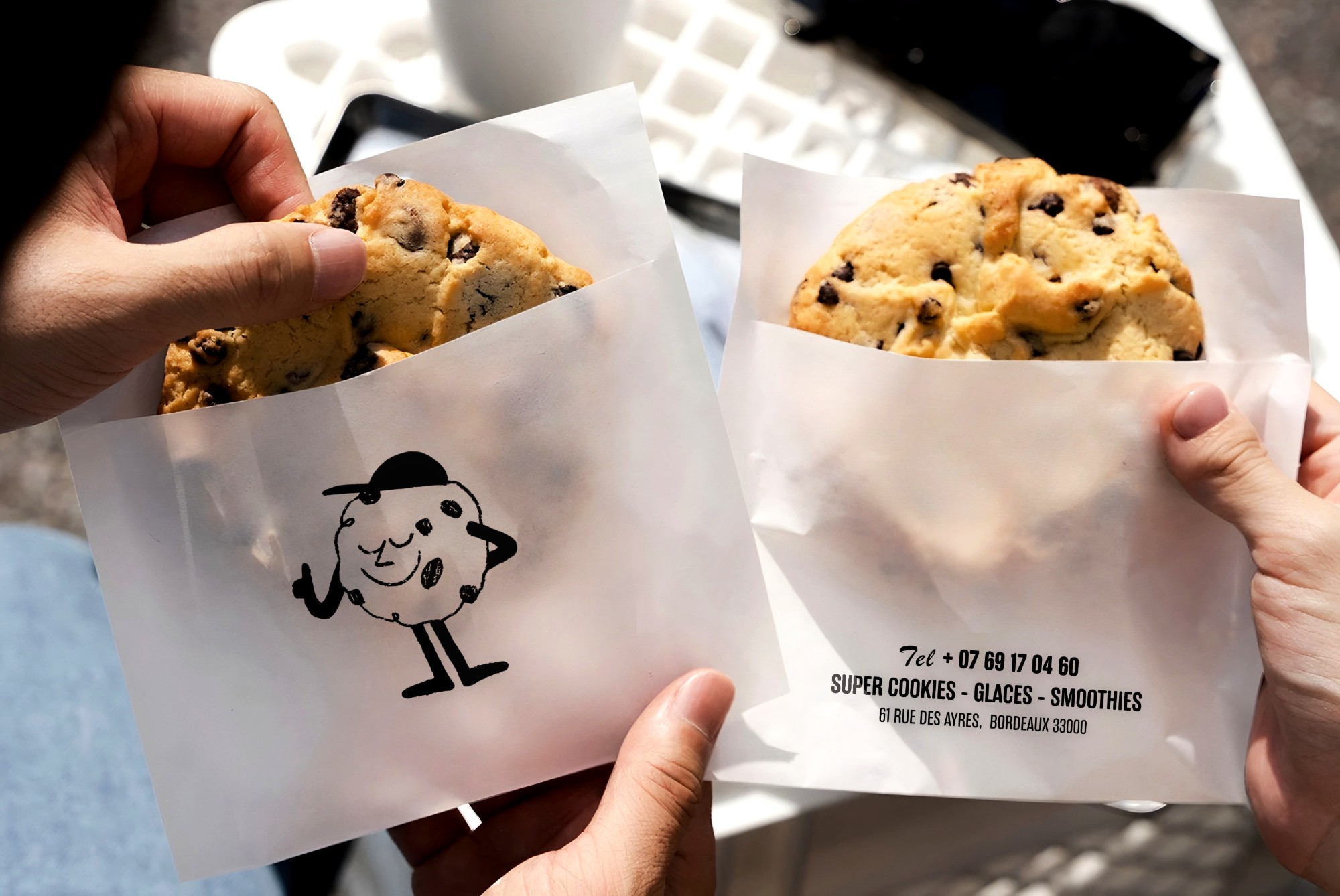 Deux cookies Batch dans leurs sachets imprimés, l’un avec la mascotte cookie, l’autre avec les coordonnées de la boutique
